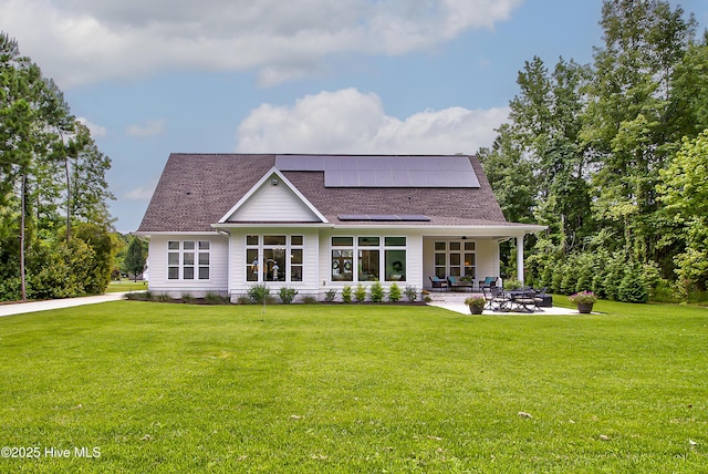 back of house featuring a yard, a patio, roof mounted solar panels, and a shingled roof