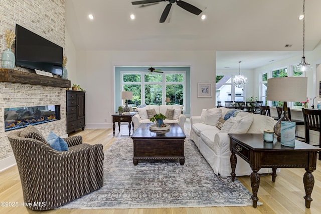 living area featuring baseboards, ceiling fan with notable chandelier, a fireplace, light wood-style floors, and high vaulted ceiling