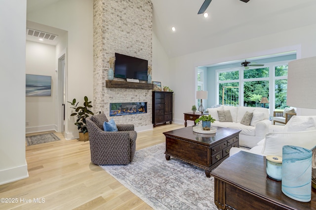 living area featuring visible vents, a large fireplace, high vaulted ceiling, and wood finished floors