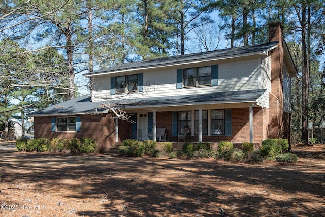 traditional-style house featuring brick siding, a porch, and a chimney