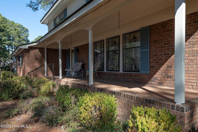 view of exterior entry with brick siding and a porch