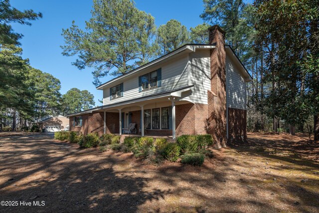 view of front of property featuring a garage, brick siding, covered porch, and a chimney