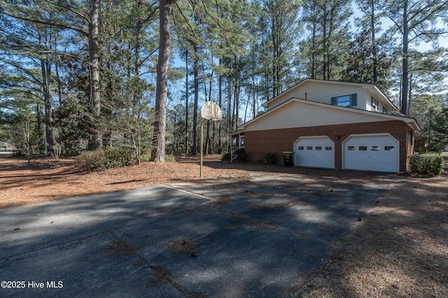 view of property exterior featuring a garage, brick siding, and driveway