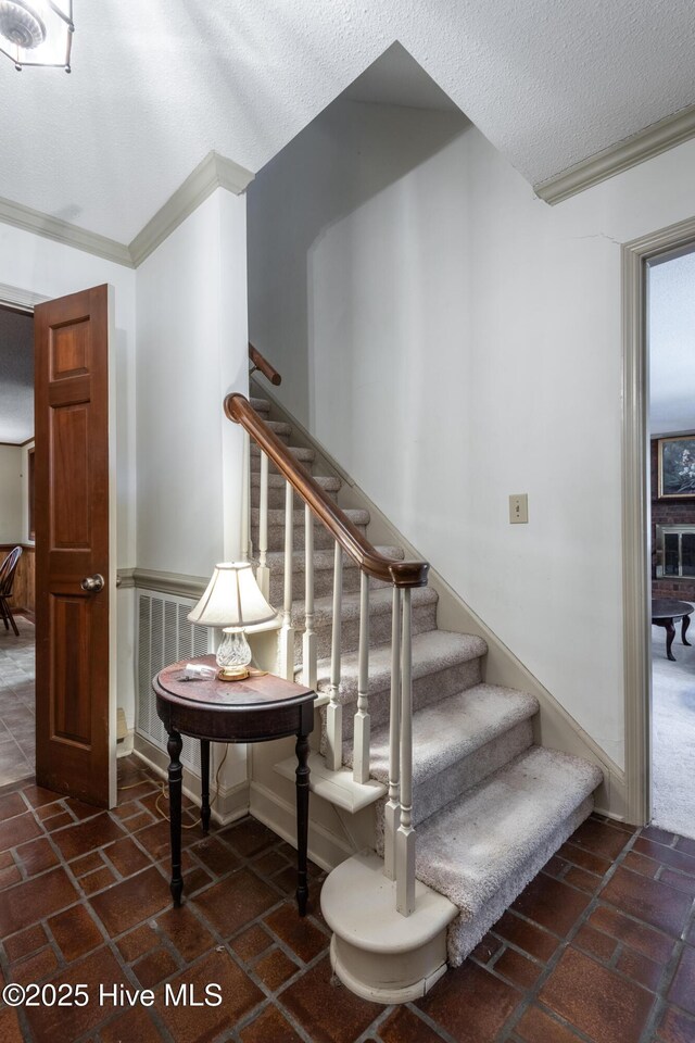 stairway with ornamental molding, visible vents, and a textured ceiling