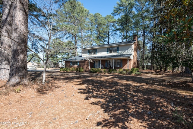 rear view of house with a porch, brick siding, and a chimney