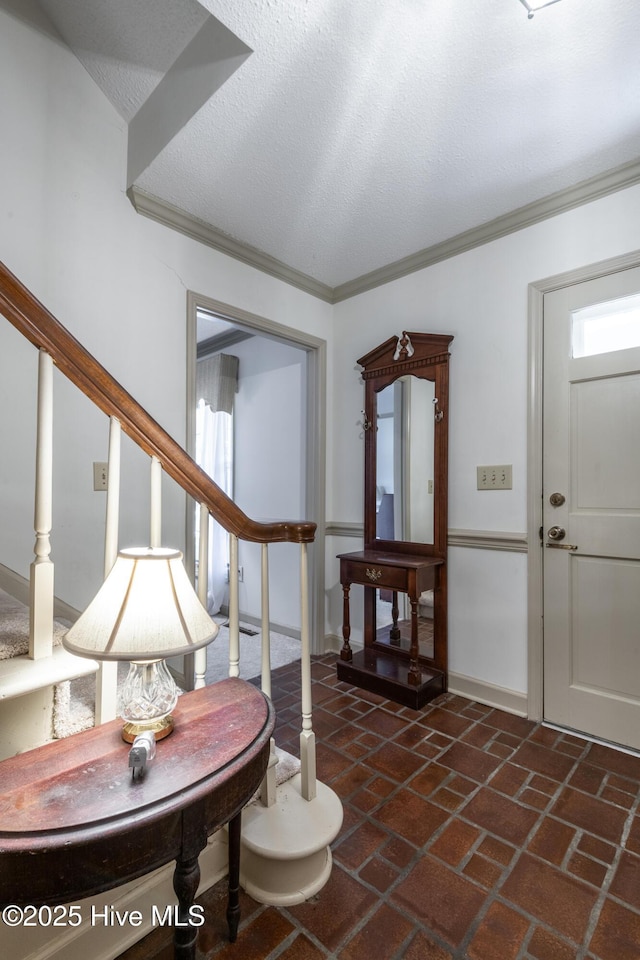 foyer entrance with a textured ceiling, stairway, brick floor, and ornamental molding