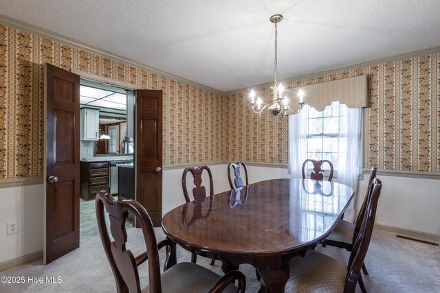 dining space with wallpapered walls, crown molding, a wainscoted wall, light colored carpet, and a textured ceiling