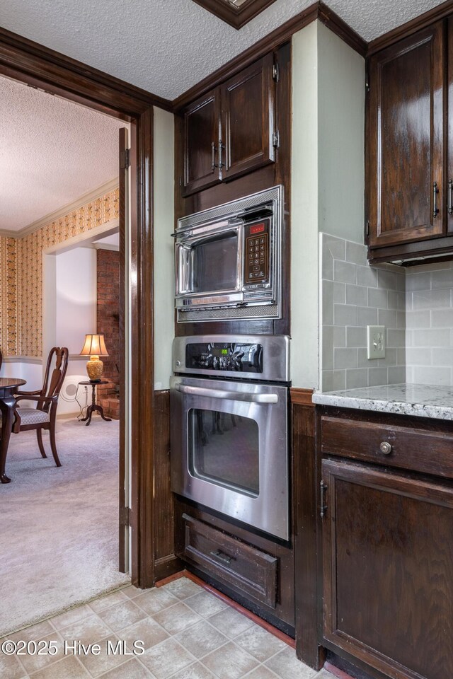 kitchen featuring built in microwave, dark brown cabinetry, light colored carpet, stainless steel oven, and a textured ceiling