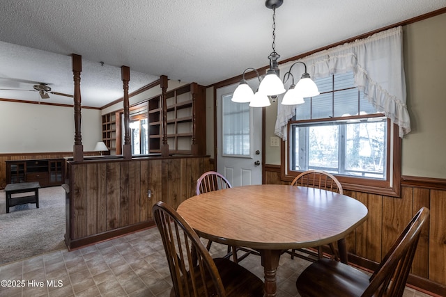 dining space featuring ornamental molding, ceiling fan with notable chandelier, a textured ceiling, wood walls, and wainscoting