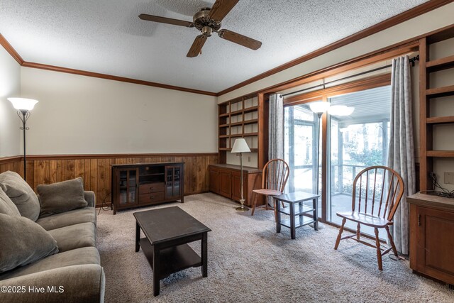 living area with carpet flooring, wainscoting, a textured ceiling, and crown molding