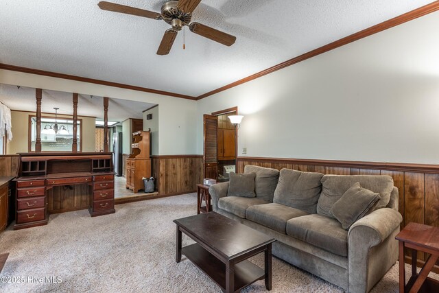 living area with wooden walls, wainscoting, ornamental molding, a textured ceiling, and light colored carpet