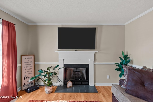 living room with a fireplace with flush hearth, a textured ceiling, wood finished floors, crown molding, and baseboards