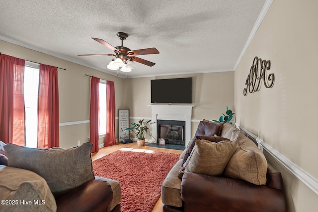 living area featuring ornamental molding, wood finished floors, a glass covered fireplace, a textured ceiling, and a ceiling fan