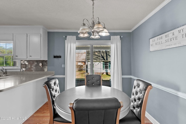 dining space featuring baseboards, ornamental molding, a textured ceiling, a notable chandelier, and light wood-type flooring