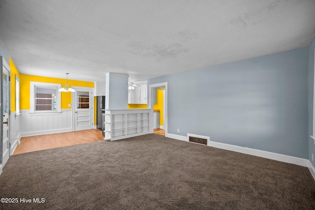 unfurnished living room featuring a notable chandelier, carpet flooring, baseboards, and visible vents