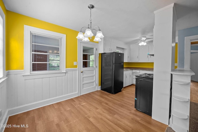 kitchen with black appliances, light wood-style floors, wainscoting, white cabinetry, and ceiling fan with notable chandelier