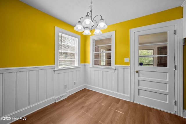 unfurnished dining area featuring a chandelier, visible vents, plenty of natural light, and wainscoting