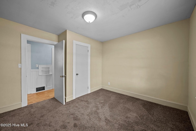 unfurnished bedroom featuring visible vents, dark carpet, and baseboards