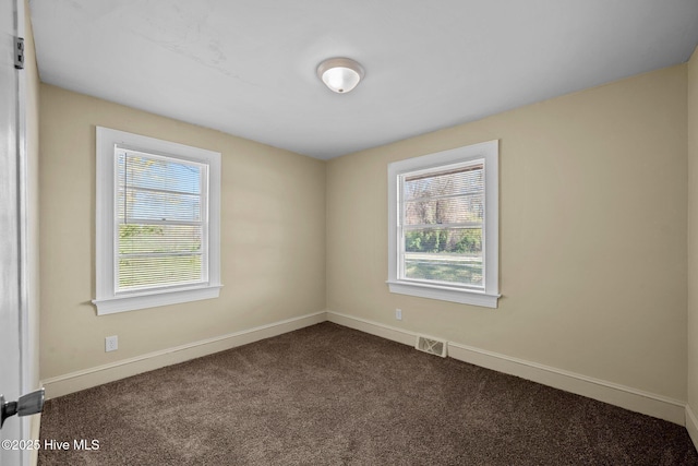 unfurnished room with dark colored carpet, visible vents, and baseboards