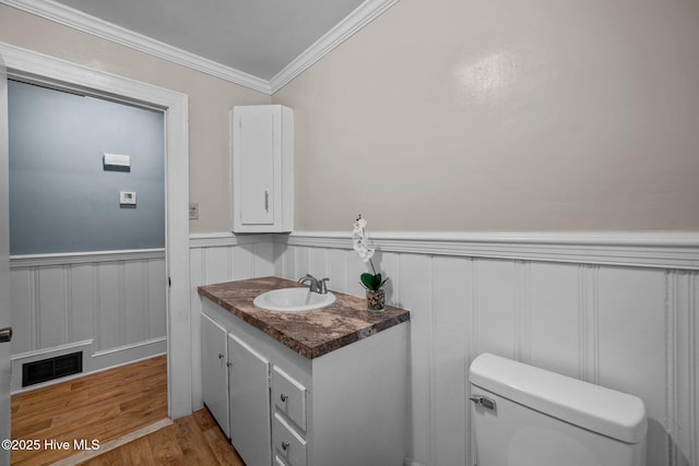 half bathroom with vanity, wood finished floors, visible vents, wainscoting, and toilet