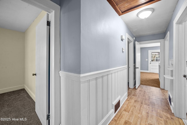 hallway featuring visible vents, a wainscoted wall, and light wood-style flooring