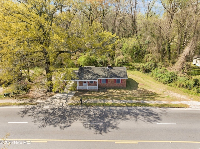 view of front of house featuring brick siding, covered porch, driveway, and a view of trees