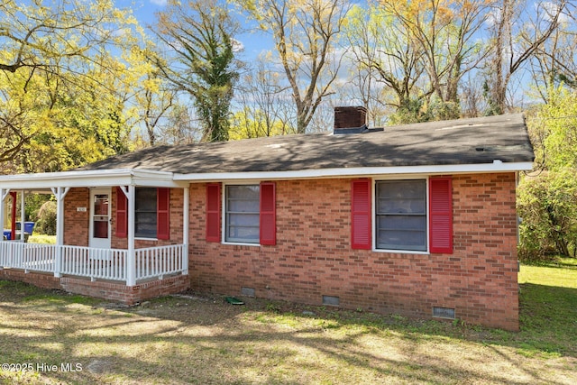 view of front of property with brick siding, a front lawn, a porch, a chimney, and crawl space