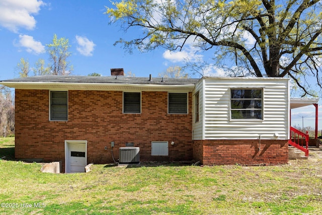 back of house featuring a yard, central AC unit, brick siding, and a chimney