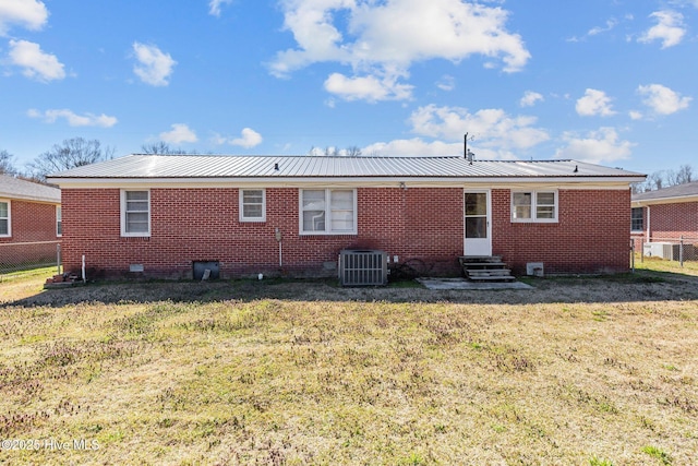 rear view of house with entry steps, central AC unit, brick siding, and a lawn