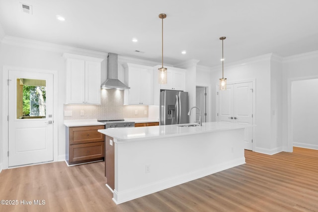 kitchen with a kitchen island with sink, wall chimney exhaust hood, a sink, stainless steel fridge, and light wood-style flooring