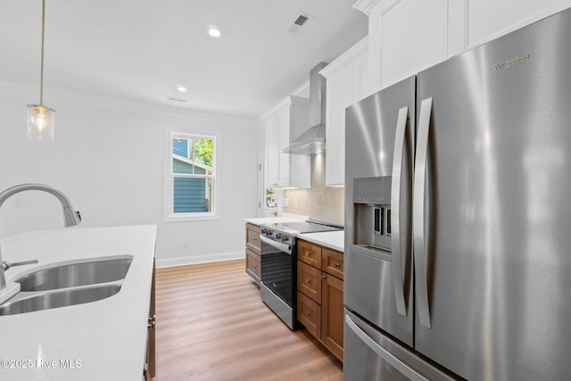 kitchen featuring a sink, light wood-style floors, light countertops, wall chimney exhaust hood, and stainless steel appliances