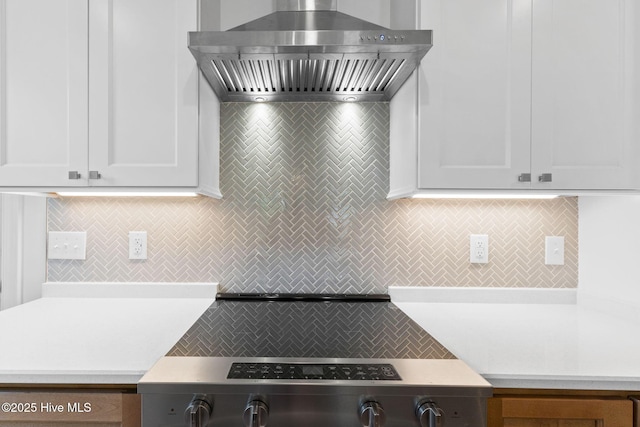 kitchen with light countertops, decorative backsplash, white cabinets, and wall chimney range hood
