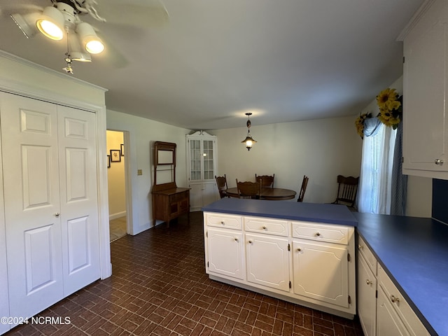 kitchen featuring brick patterned floor, dark countertops, a peninsula, and white cabinets