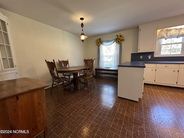 kitchen with white cabinetry, dark countertops, hanging light fixtures, and brick patterned floor