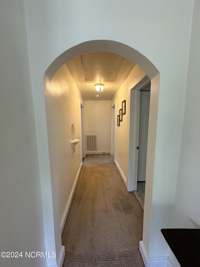 corridor with visible vents, baseboards, attic access, carpet flooring, and arched walkways