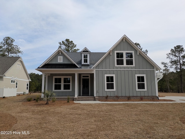 view of front of property with a front yard, covered porch, board and batten siding, and roof with shingles