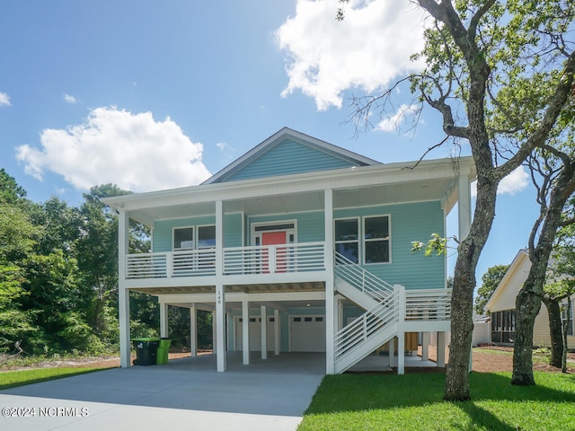 beach home with a front yard, stairway, covered porch, concrete driveway, and a garage