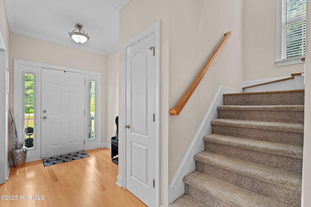 foyer entrance featuring baseboards, wood finished floors, ornamental molding, and stairs