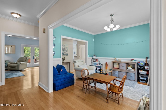 dining space featuring wood finished floors, french doors, wainscoting, crown molding, and a chandelier