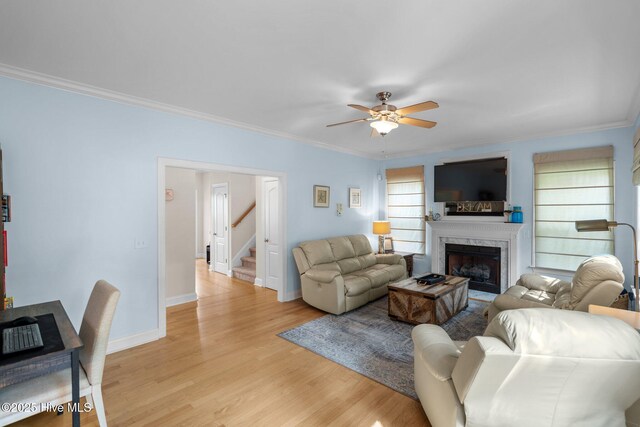 living room featuring crown molding, stairway, a fireplace, and light wood finished floors