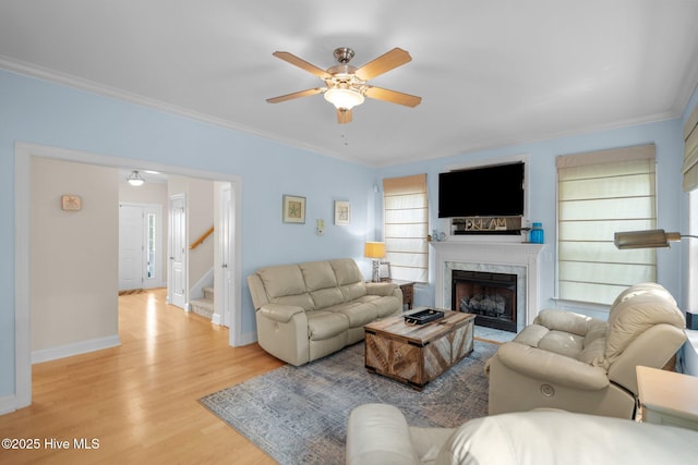 living room featuring stairs, crown molding, a fireplace, and light wood finished floors