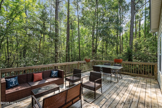 deck with outdoor dining space, an outdoor living space, and a view of trees