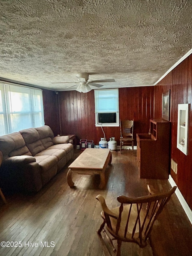 living area featuring ceiling fan, wooden walls, wood finished floors, and a textured ceiling