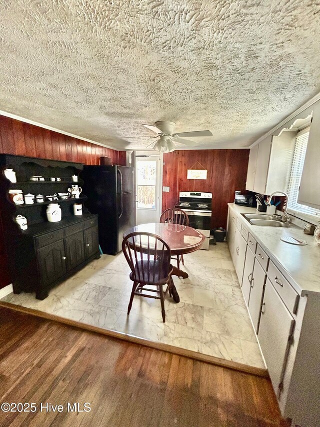 dining room featuring wooden walls, a textured ceiling, a ceiling fan, and light wood-style floors