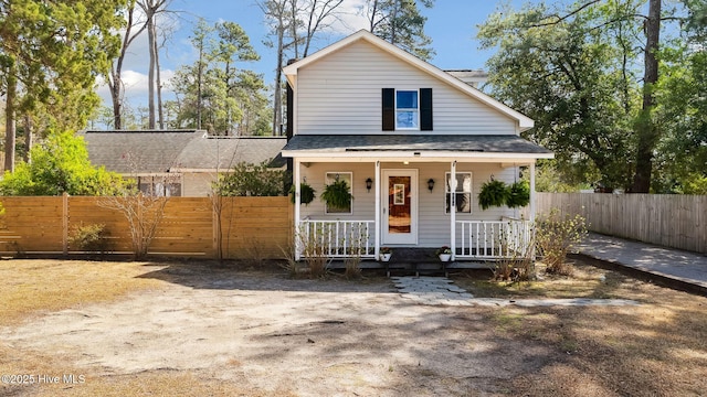 view of front of house with a porch, roof with shingles, and fence