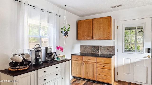 kitchen featuring visible vents, backsplash, dark countertops, wood finished floors, and a textured ceiling