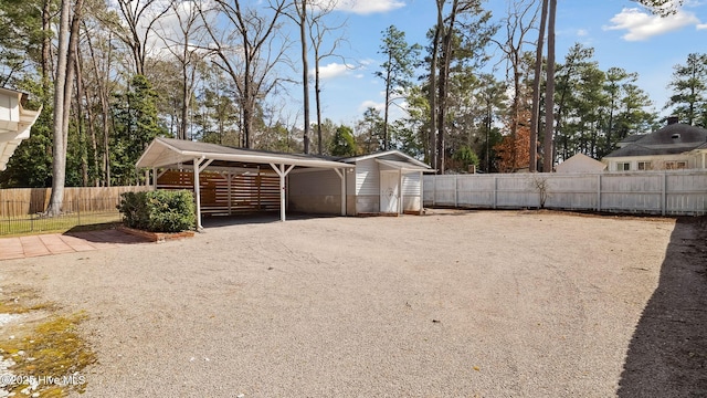 exterior space featuring a detached carport, gravel driveway, an outdoor structure, and fence