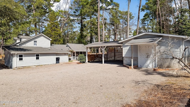 back of property with gravel driveway, an outbuilding, and a shingled roof