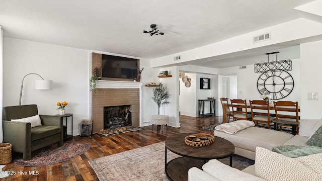 living room with visible vents, a brick fireplace, and wood finished floors