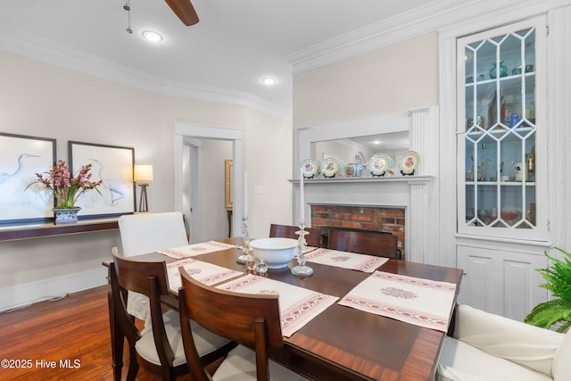 dining room featuring a ceiling fan, wood finished floors, baseboards, a fireplace, and ornamental molding